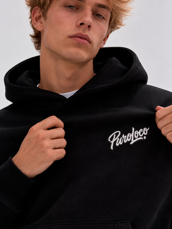 Sudadera oversize negra con capucha y logo bordado 'Puro Loco' en el pecho, modelo masculino.