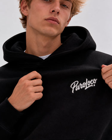 Sudadera oversize negra con capucha y logo bordado 'Puro Loco' en el pecho, modelo masculino.