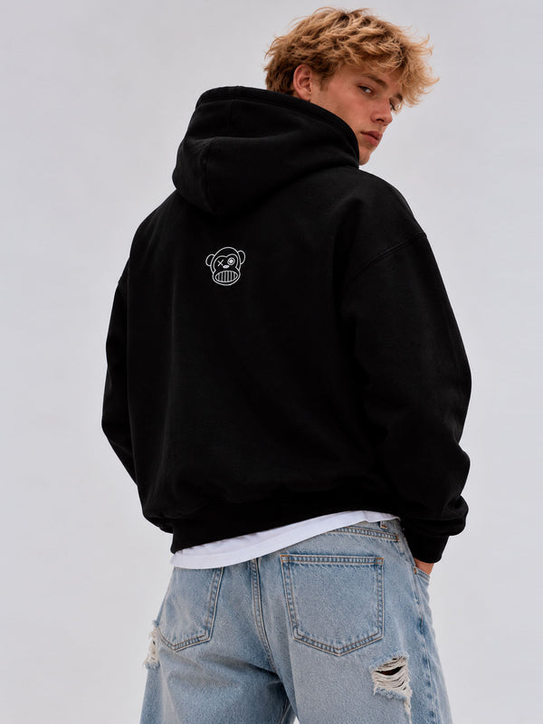 Sudadera oversize negra con capucha, diseño de logo de mono en la parte posterior, modelo masculino de cabello rizado.