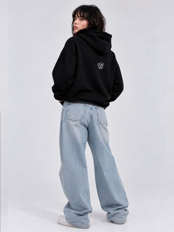 Sudadera oversize negra con capucha, diseño en la parte trasera, combinada con pantalones anchos de mezclilla.