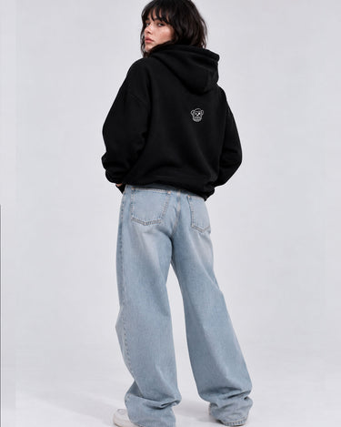 Sudadera oversize negra con capucha, diseño en la parte trasera, combinada con pantalones anchos de mezclilla.