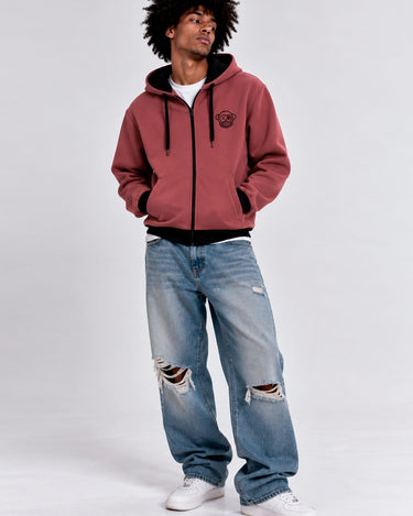 Sudadera con cremallera color vino, con capucha y logo en el pecho, combinada con jeans desgastados.