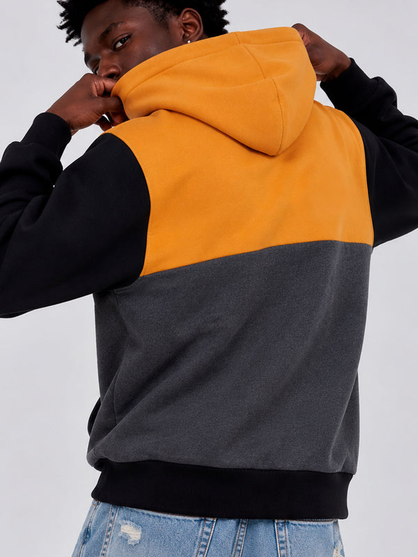 Sudadera con capucha en colores mostaza, negro y gris oscuro, vista trasera, con detalles de costura.