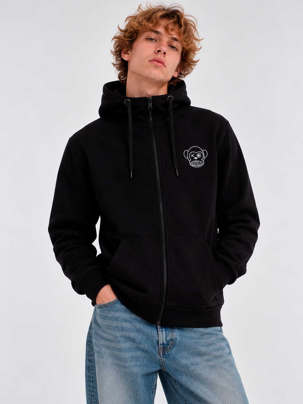 Sudadera negra con cremallera, capucha y logo de mono en el pecho, modelo masculino con jeans claros.