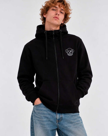 Sudadera negra con cremallera, capucha y logo de mono en el pecho, modelo masculino con jeans claros.