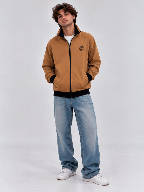 Chaqueta sin capucha color caramelo con logo de Loco Monky, combinada con jeans claros y zapatillas blancas.