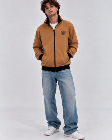 Chaqueta sin capucha color caramelo con logo de Loco Monky, combinada con jeans claros y zapatillas blancas.