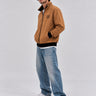 Chaqueta sin capucha color caramelo con logo en el pecho, combinada con jeans claros y zapatillas blancas.