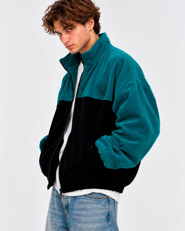 Chaqueta de pana oversize en negro y azul océano, con cierre y cuello alto, estilo unisex.