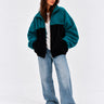 Chaqueta de pana oversize unisex en negro y azul océano, con logo en el pecho y pantalones de mezclilla claros.