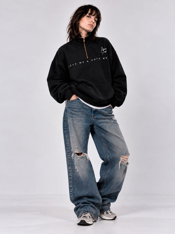 Sudadera oversize negra con cremallera y texto 'LOVE ME & HATE ME', combinada con jeans desgastados.