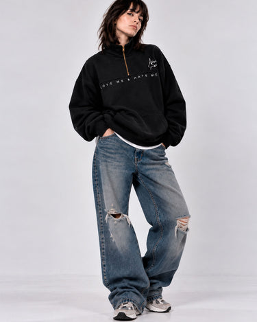 Sudadera oversize negra con cremallera y texto 'LOVE ME & HATE ME', combinada con jeans desgastados.