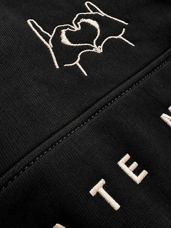 Sudadera negra con diseño bordado de manos formando un corazón y texto en la parte inferior.