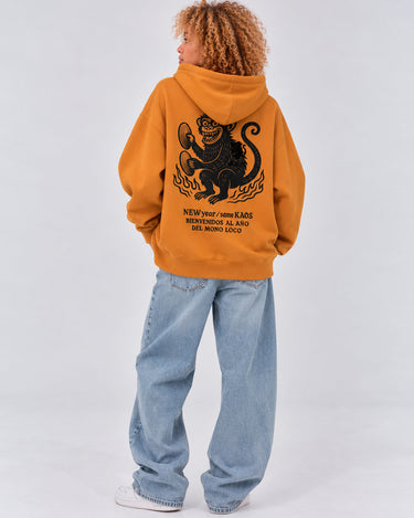 Sudadera unisex mostaza con diseño de mono en la espalda y capucha, pantalones de mezclilla claros.