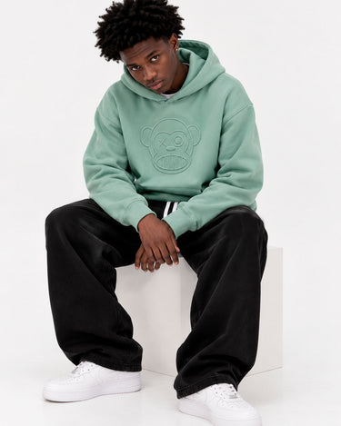 Sudadera unisex verde suave con capucha y diseño de mono en el pecho, pantalones negros y zapatillas blancas.