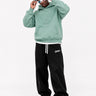 Sudadera verde suave con capucha y diseño de mono en relieve, pantalones negros y gafas de sol coloridas.