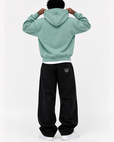 Pantalón oversize negro con logo en la parte trasera, combinado con sudadera verde claro, vista trasera.