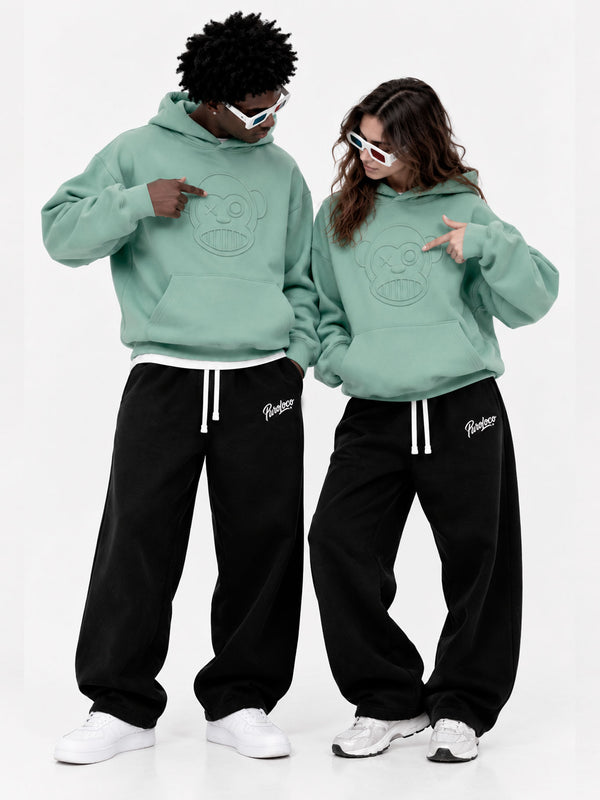 Pantalones oversize negros con cordones, combinados con sudaderas verdes, dos modelos posando juntos.