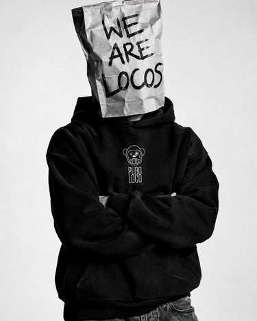 Sudadera negra con capucha, logo 'PURO LOCO' en el pecho, persona con bolsa de papel en la cabeza.