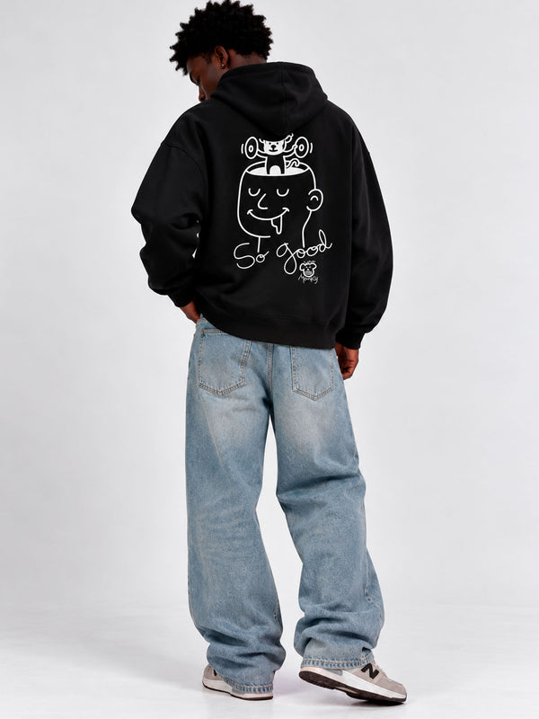 Sudadera negra con capucha, diseño gráfico en la espalda, jeans claros, modelo de pie de espaldas.
