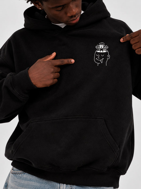Sudadera negra con capucha, diseño gráfico en el pecho, persona señalando el logo.