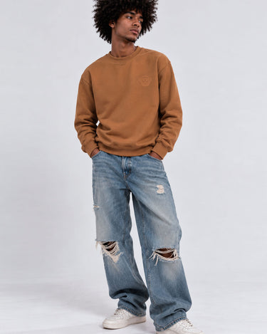 Sudadera color caramelo con logo en el pecho, jeans desgastados y zapatillas blancas, fondo gris claro.