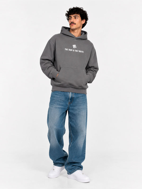 Sudadera unisex de color gris profundo con capucha y texto blanco en el pecho, pantalones vaqueros azules.