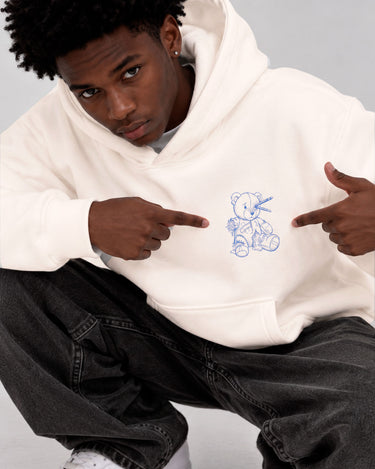 Sudadera blanca unisex con un diseño de oso de peluche azul en el pecho, modelo señalando el diseño.