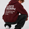 Sudadera unisex color burdeos con capucha, texto blanco en la espalda, modelo agachado en fondo gris.