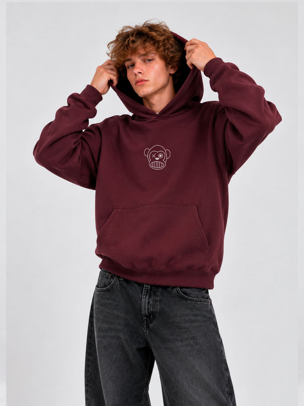 Sudadera unisex color burdeos con capucha y logo de mono en el pecho, modelo masculino con cabello rizado.