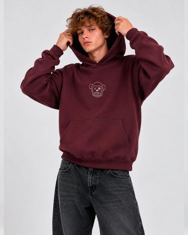 Sudadera unisex color burdeos con capucha y logo de mono en el pecho, modelo masculino con cabello rizado.