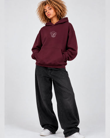 Sudadera unisex color burdeos con capucha y logo de mono en el pecho, combinada con pantalones negros amplios.