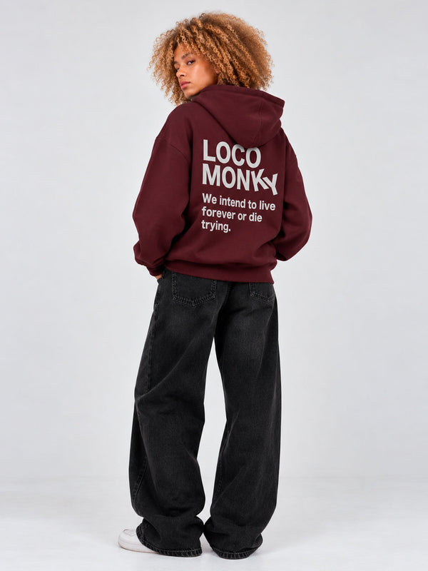 Sudadera unisex color burdeos con capucha, texto en la parte posterior en gris, pantalones negros amplios.