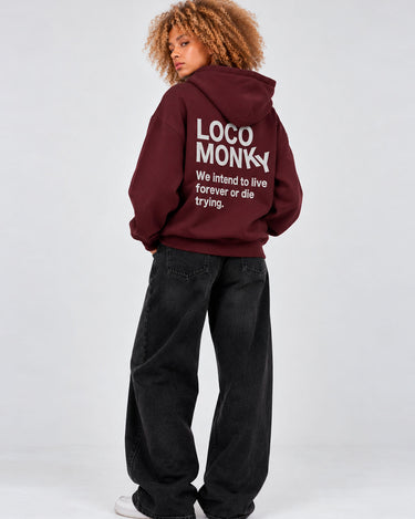 Sudadera unisex color burdeos con capucha, texto en la parte posterior en gris, pantalones negros amplios.