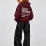 Sudadera unisex color burdeos con capucha, texto en la parte posterior en gris, pantalones negros amplios.